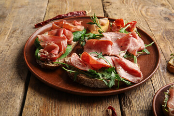 Plate of tasty bruschettas with ham on wooden background