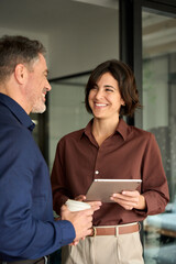 Executive team of two business people working talking using tablet tech in corporate office. Happy...