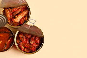 Opened tin cans with fish in tomato sauce on beige background