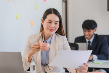 Obraz premium Asian Businesswoman Reviewing Documents with Coffee