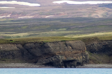 Scenic landscape showing layered cliff face, green meadows and snowy mountains in Iceland