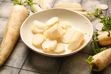 Bowl with slices of fresh daikon radish on grey tile background