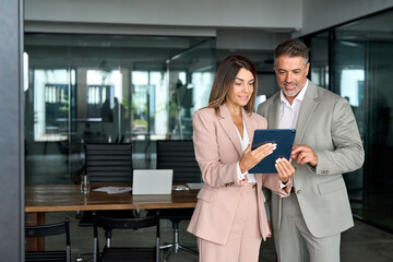 Two busy older professional corporate business executives man and woman wearing suits working on...