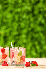 Glasses of strawberry lemonade on white wooden table outdoors