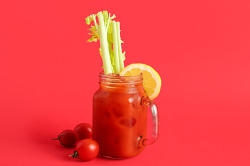 Mason jar of bloody mary with celery and lemon on red background