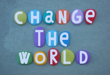Change the world, creative social slogan composed with multi colored hand painted stone letters over green sand
