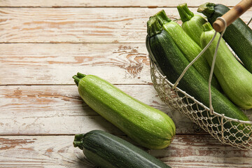 Basket with fresh green zucchini on white wooden background