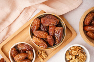 Bowls with dried dates and nuts on light background