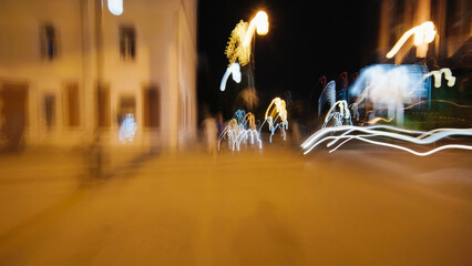 Urban nightscape showing blurred light trails streaming across dark street, revealing dynamic...