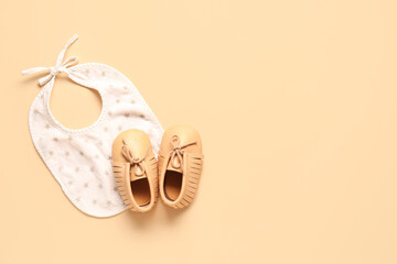 Stylish baby shoes with bib on beige background