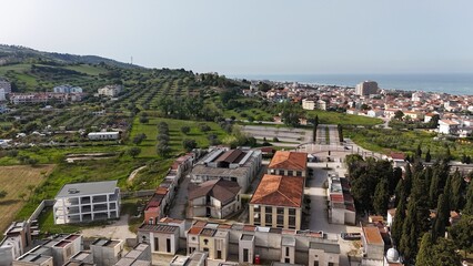 This aerial view captures a modern Italian cemetery, featuring an array of distinct mausoleums and tombs nestled among cypress trees, revealing organized pathways and a solemn, architectural landscape