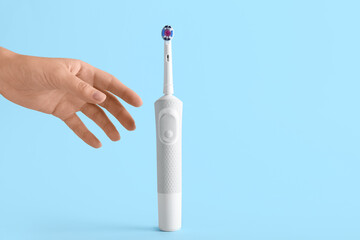 Female hand with electric toothbrush on blue background.