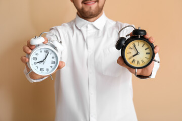 Young businessman with alarm clocks on beige background, closeup. Time management concept
