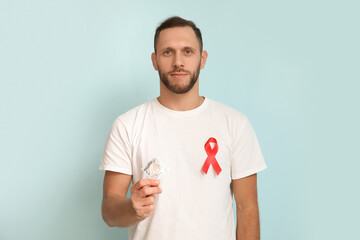 Young man with red ribbon and condom on blue background. AID awareness concept