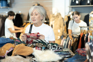 Happy mature woman looking at second hand clothes in large clothing shop