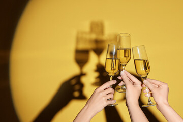 Female hands with glasses of champagne on yellow background