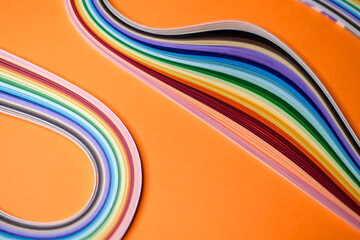Colorful quilling paper strips arranged in smooth, flowing curves on a vibrant orange background.