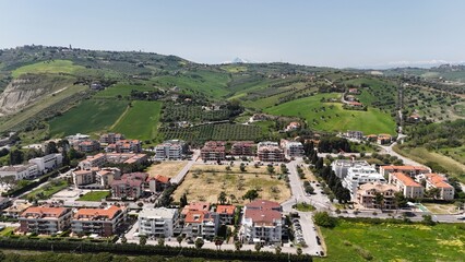 Fototapeta premium An aerial view captures the Italian coastal town of Roseto degli Abruzzi, nestled between modern buildings and a lush, green hillside under a clear sky.