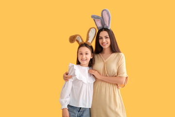 Happy little girl and her mother in bunny ears on yellow background