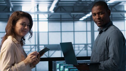 Portrait of happy system administrators in data center using devices, verifying firewall...
