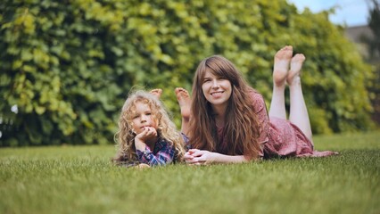 Obraz premium Mother with daughter relaxing on green lawn, sharing peaceful summer moment in backyard