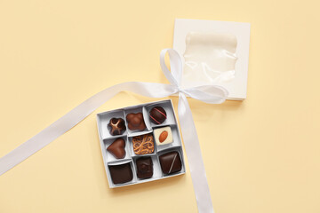 Box with tasty chocolate candies on yellow background