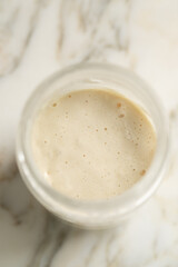 active sourdough starter in glass jar on white marble counter