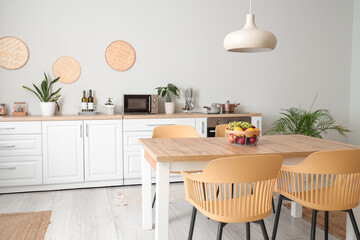 Interior of modern kitchen with white counters, dining table, fruits, chairs and lamp