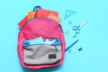 Modern school backpack with different stationery supplies on blue background
