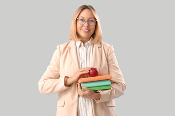 Mature female math teacher with books and apple on grey background