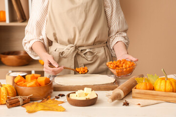 Woman preparing tasty pumpkin strudel on table in kitchen