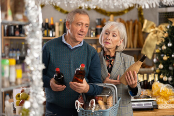 While shopping on eve of New Year holidays, elderly couple is interested in alcoholic beverages. They bought set of shopping cart products, choose right drink for party and feast