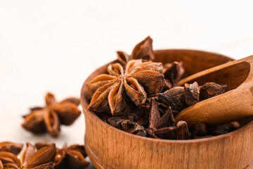 Wooden bowl with aromatic star anise and scoop on light background, closeup