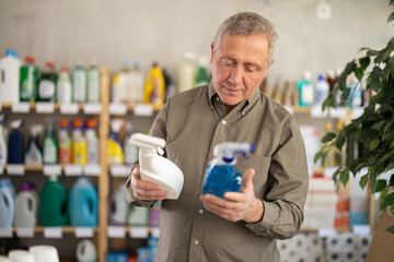 European buyer holds cleaning sprays for the house in his hands and reads the instructions. Elderly man buying spray to clean tables, surfaces and tiles