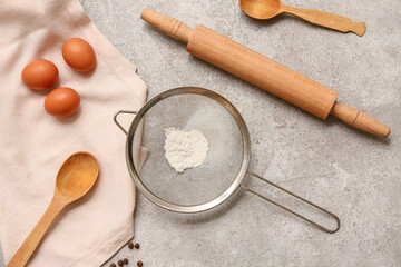 Metal sieve with flour, spoons, rolling pin and chicken eggs on grunge background