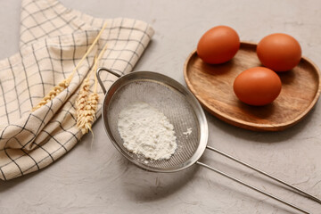 Metal sieve with flour, napkin and chicken eggs on grunge background