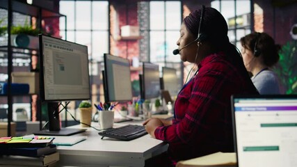 IT support specialist at PC in office helping customers during call, troubleshooting errors. Tech support agent at desk looking at computer monitor, fixing technical issues for clients, camera B