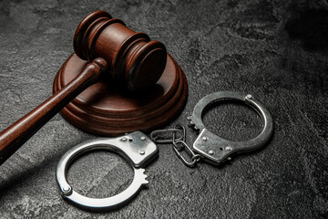 Handcuffs with judge's gavel on dark background, closeup
