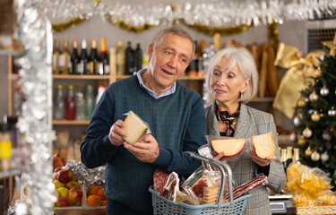 Elderly couple is looking at cheese in store. Market visitors choose from several varieties, consult and evaluate freshness of product, are interested in manufacturer and read label information