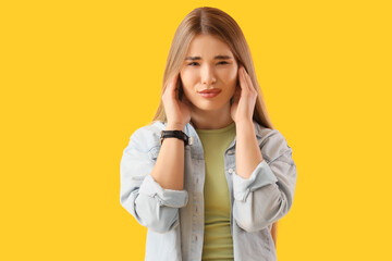 Young woman suffering from loud noise on yellow background