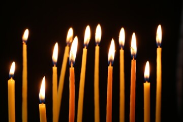 Many burning church candles on dark background, closeup