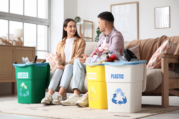 Young couple with sorted rubbish in garbage bins sitting on sofa at home. Global Recycling Day