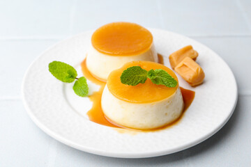 Tasty puddings with caramel sauce served on white tiled table, closeup
