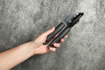 Woman holding can opener against grey background, closeup