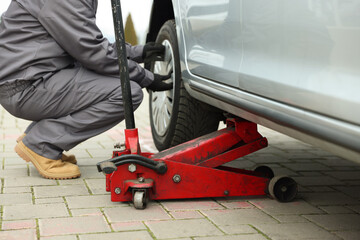Fototapeta premium Car lifted by scissor jack. Auto mechanic changing wheel outdoors, closeup