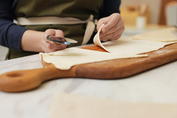 Woman cutting dough at light table, closeup. Making croissants