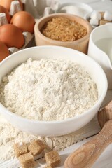 Rolling pin and ingredients for dough on white wooden table, closeup