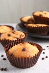 Delicious muffin with chocolate chips on light grey table, closeup