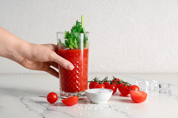Female hand with glass of bloody mary, celery, tomatoes, salt and ice cubes on marble table