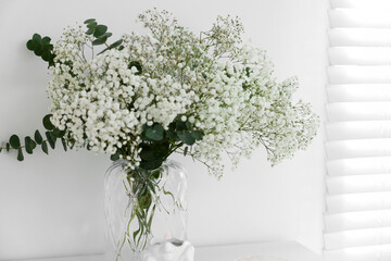 Bouquet of beautiful gypsophila flowers and eucalyptus branches in vase near white wall, closeup